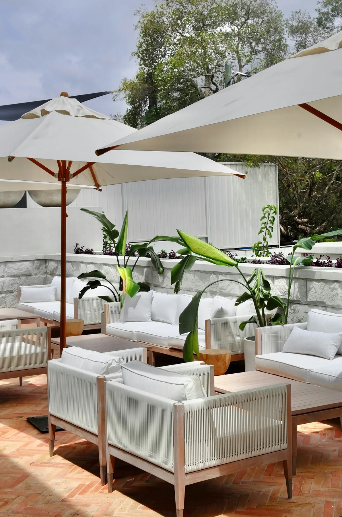 Outdoor hospitality lounge with white seating, greenery and parasols